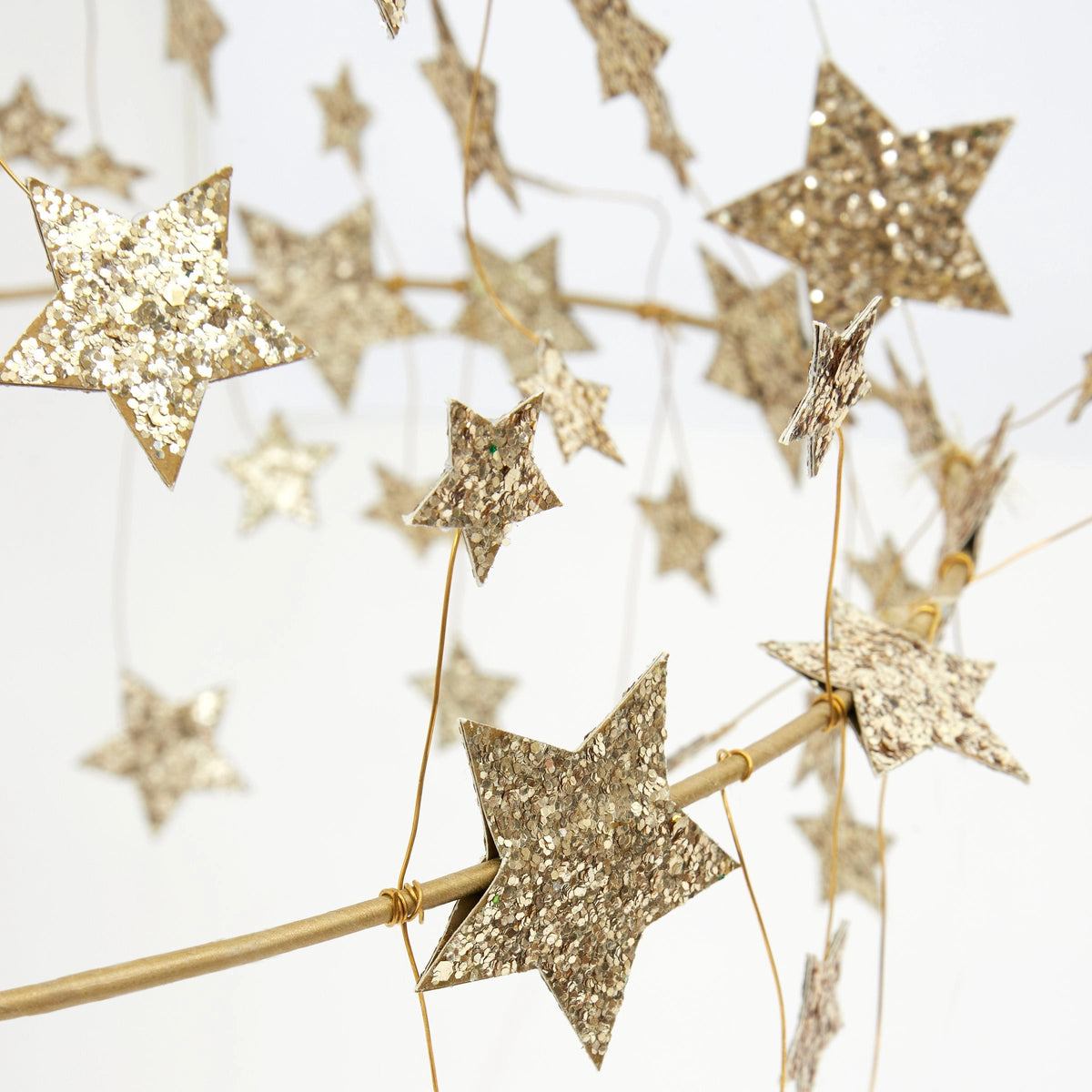 Close-up of Faire’s Gold Sparkle Star Chandelier, featuring glittery gold stars suspended from thin wires for a whimsical, pajaki-inspired decoration against a light background.