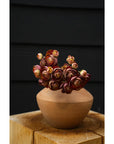 The Faire Ranunculus Bouquet features dark pink and cream faux ranunculus stems beautifully arranged in a round brown clay vase, displayed on wood with a black background.