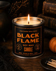 Faire Black Flame Soy Candle with oud scent, lit on a wood table in a cozy autumn setting, Bungalow Furniture & Accessories.