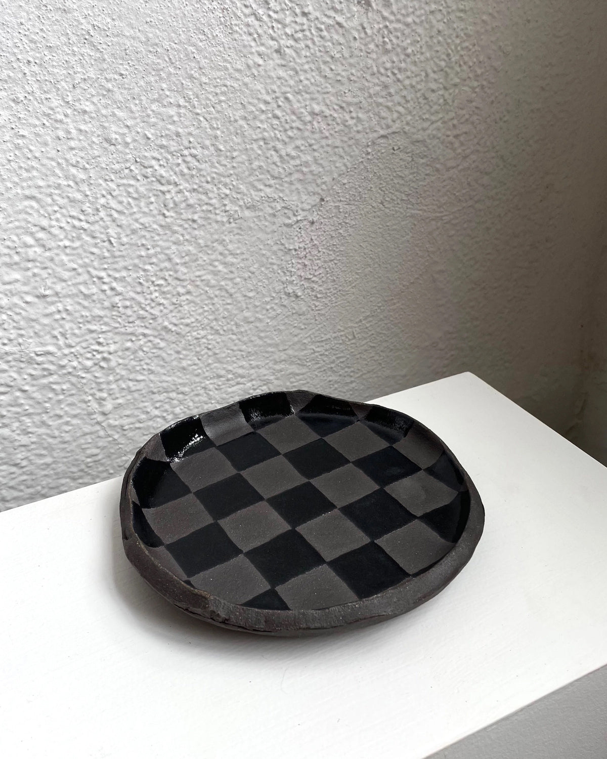 Round glossy black check snack plate by Bungalow Furniture, displayed on a white surface near a textured wall.