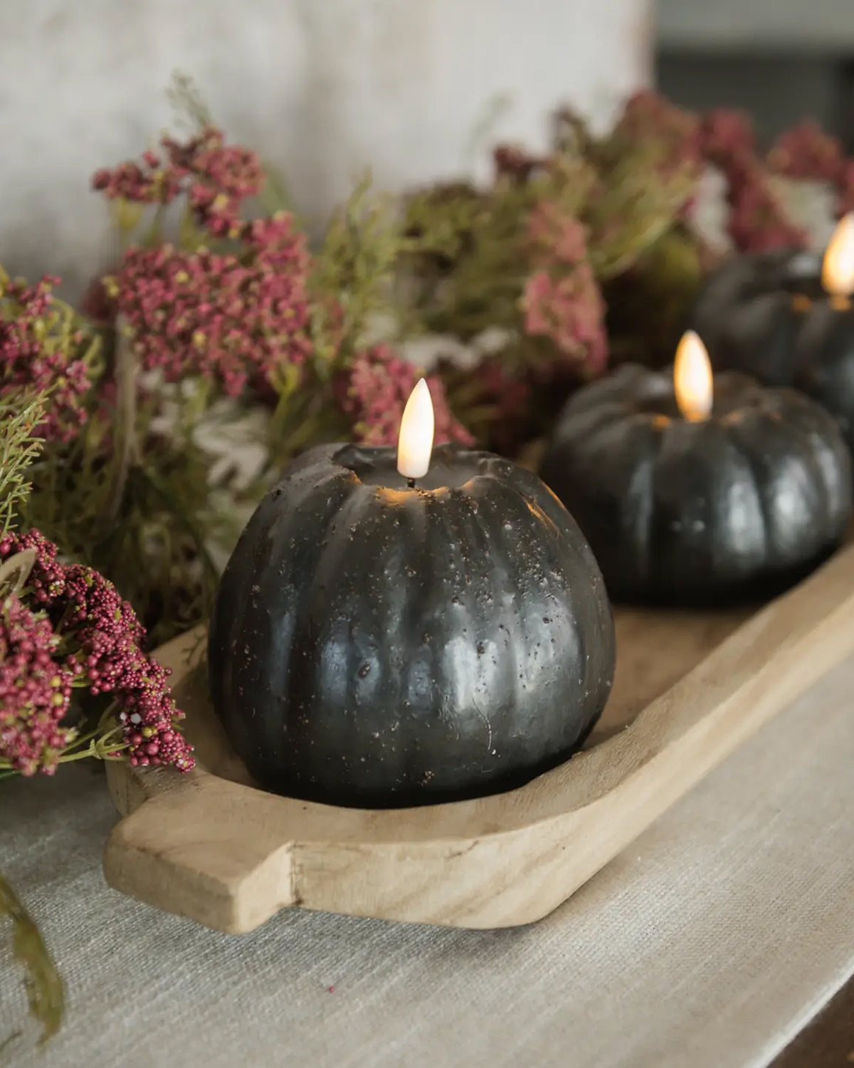 Set of three black 3D flame pumpkin candles by Faire on a tray with pink and green dried flowers.