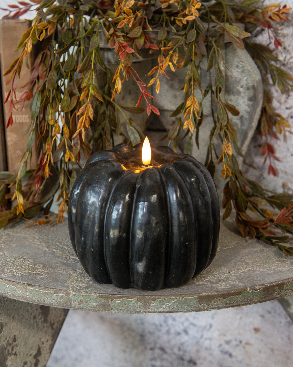 Black 3D flame pumpkin candle by Faire glows on rustic wood with fall garland, perfect for cozy autumn décor.