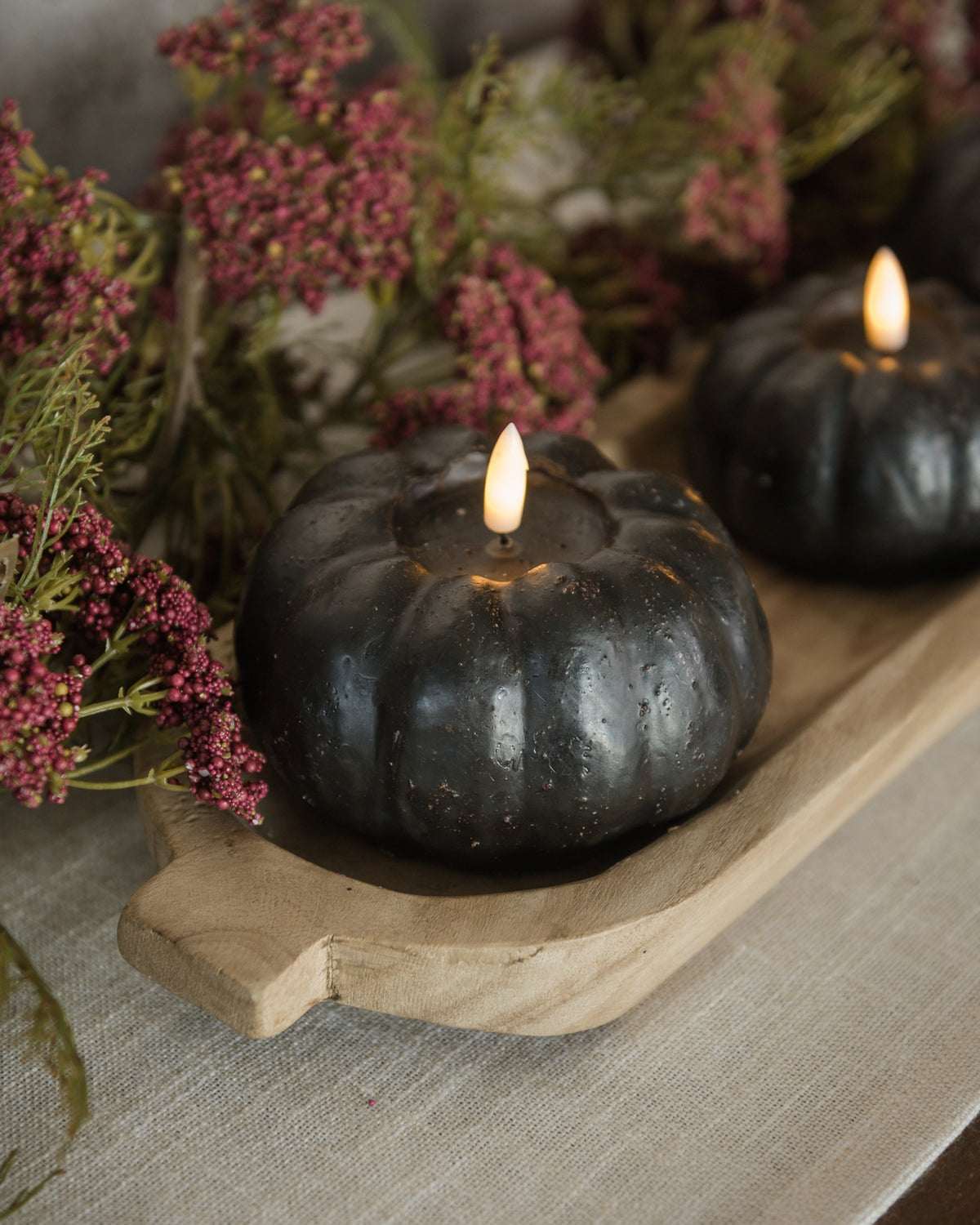 Black pumpkin-shaped candle with 3D flame by Faire, displayed on a tray with pink dried flowers, 3.5″, 6-hour timer.