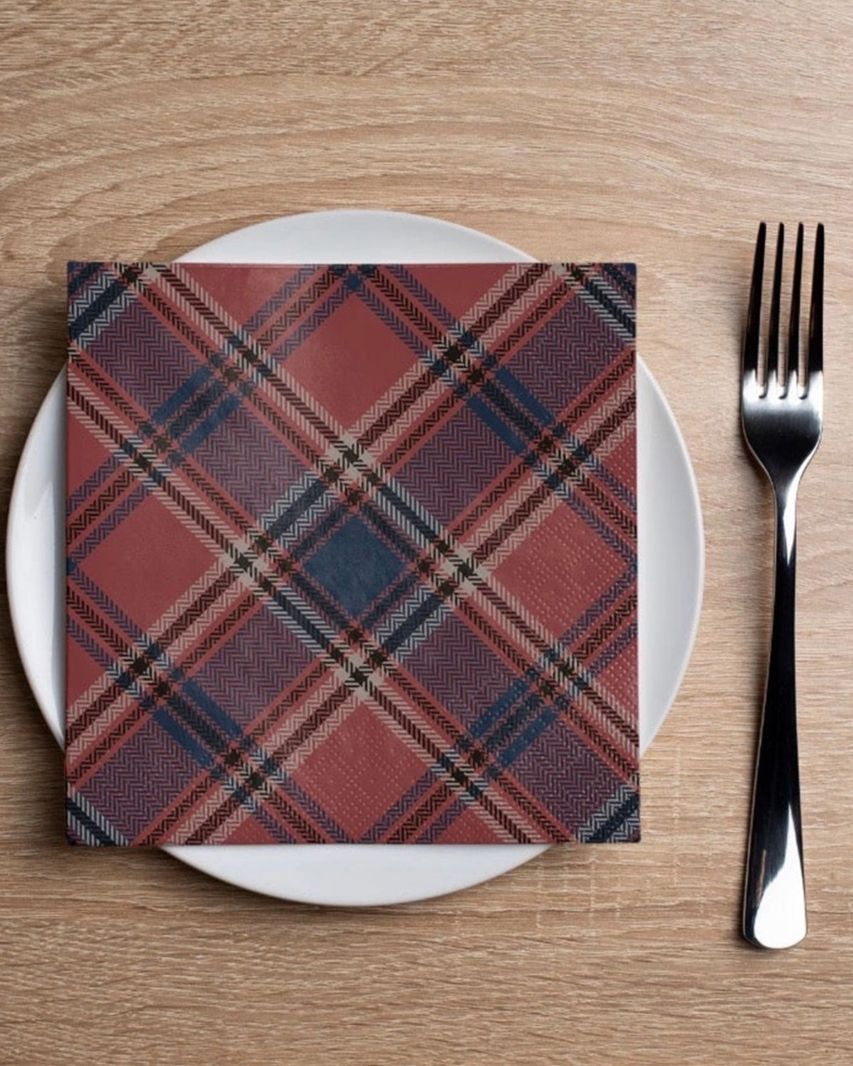 Plaid cocktail napkin by Faire on a white plate with fork, styled on a wooden table for Bungalow Furniture & Accessories.
