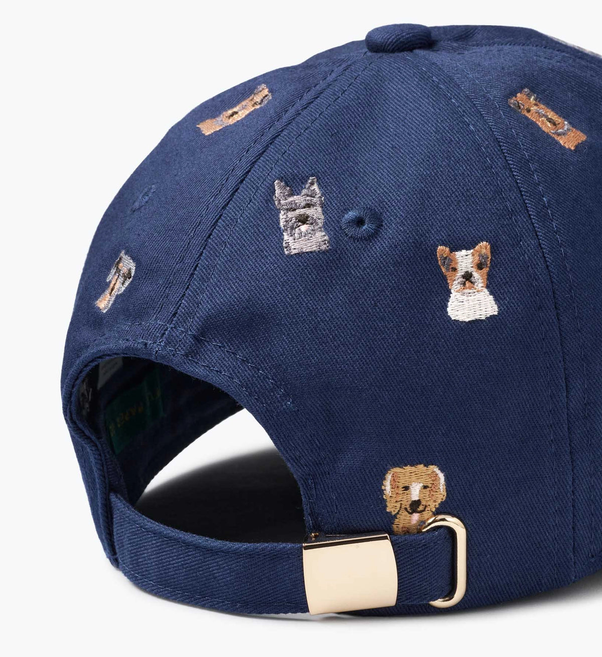 The Faire Dog Days Baseball Cap is navy blue with an adjustable strap, metal buckle, and embroidered dog faces on the back.