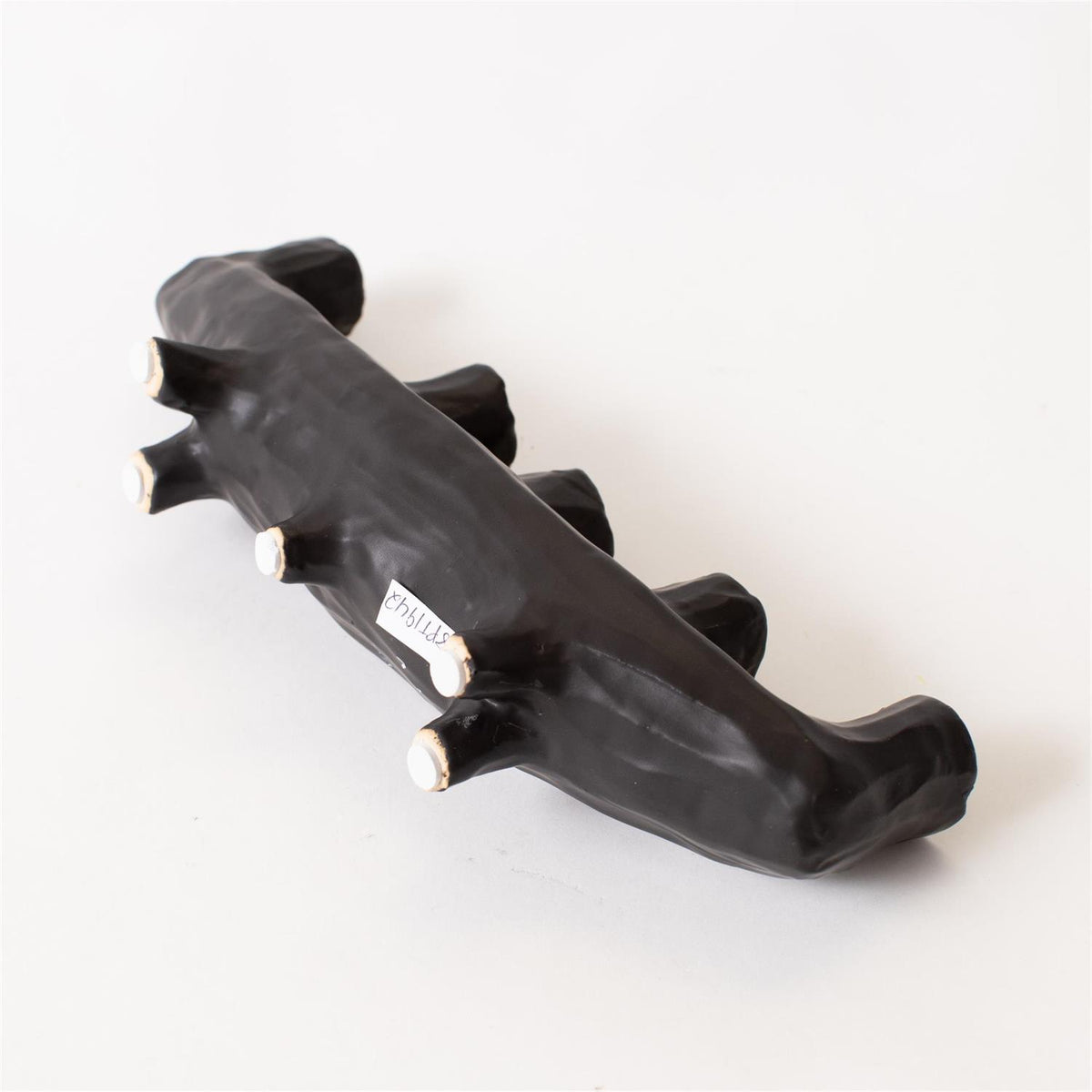 The Black Crescent Shape by Faire is a black, abstract ceramic sculpture with five rounded knobs, displayed on a white background. A small text label is attached to one side, making it a unique decor piece.