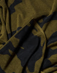 A close-up of the Typical Wild Camouflage Bath Towel highlights its soft, textured green and black design with overlapping folds and subtle shadows.