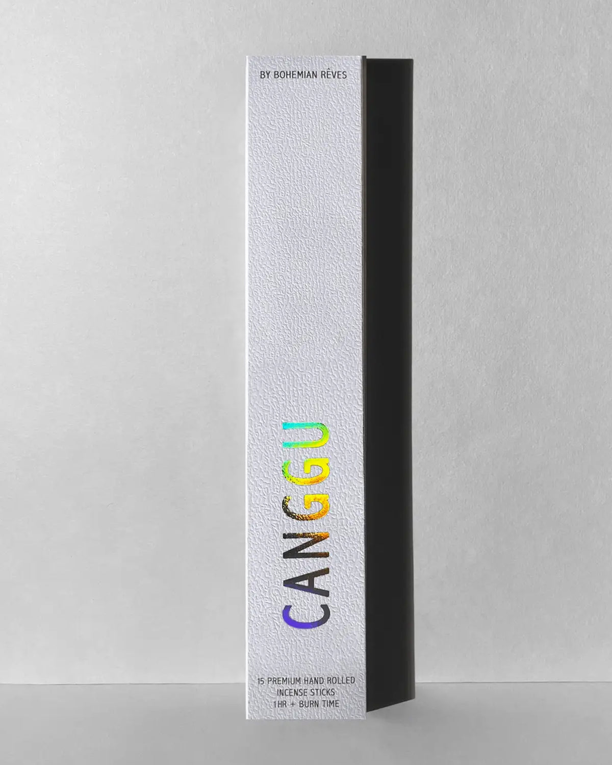 A tall, textured white box from Faire stands upright with "CANGGU" in rainbow letters down the front, suggesting Exotic & Alluring Canggu Incense Sticks inside with amber resin and cedarwood notes. The background is plain and neutral.