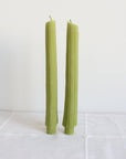 Two Faire Celery Beeswax Candles, handmade in Los Angeles, stand upright on a white cloth against a plain white background.