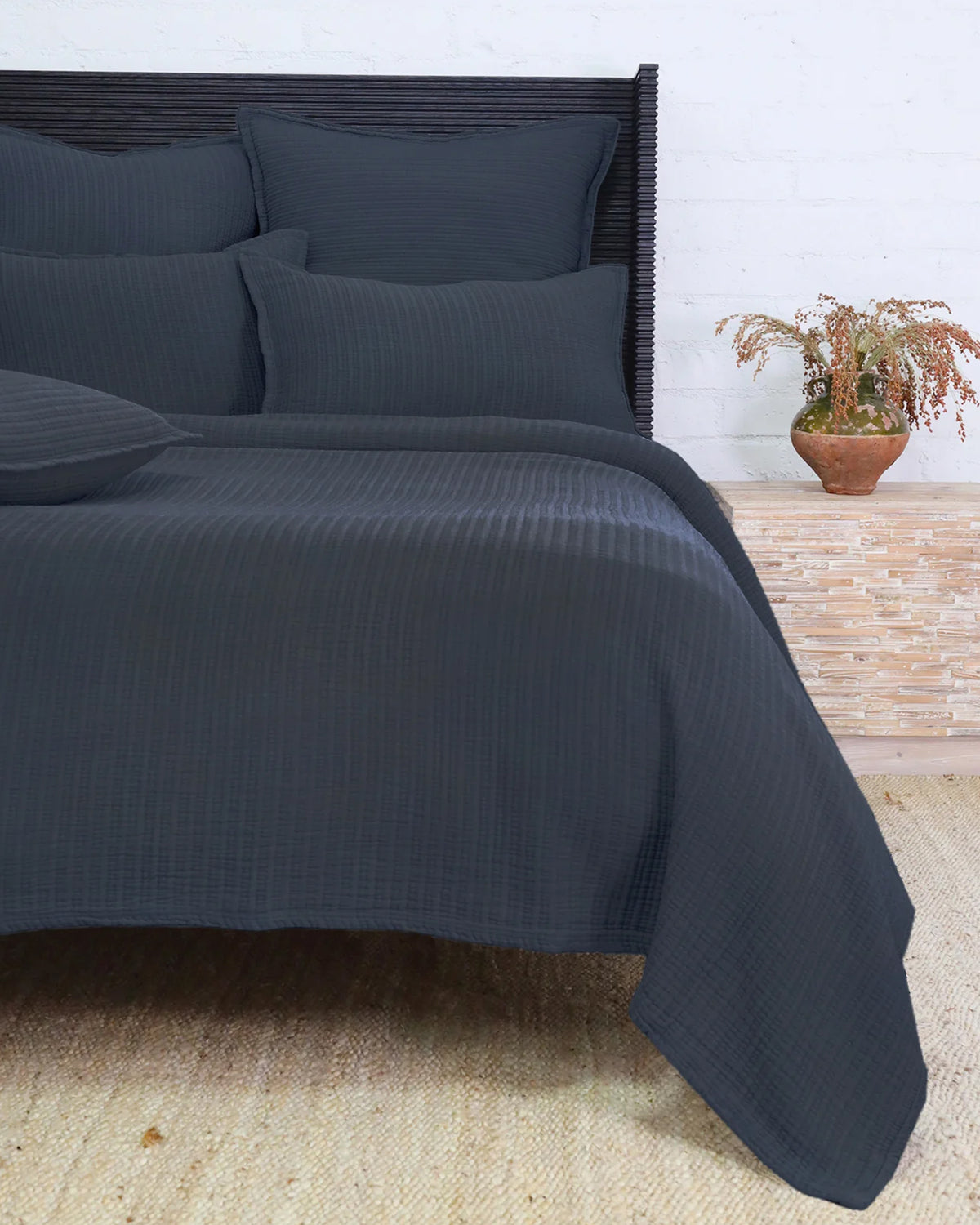 Dark gray Chatham Matelasse Queen bedding by POM POM on a bed beside a small table with a potted plant.