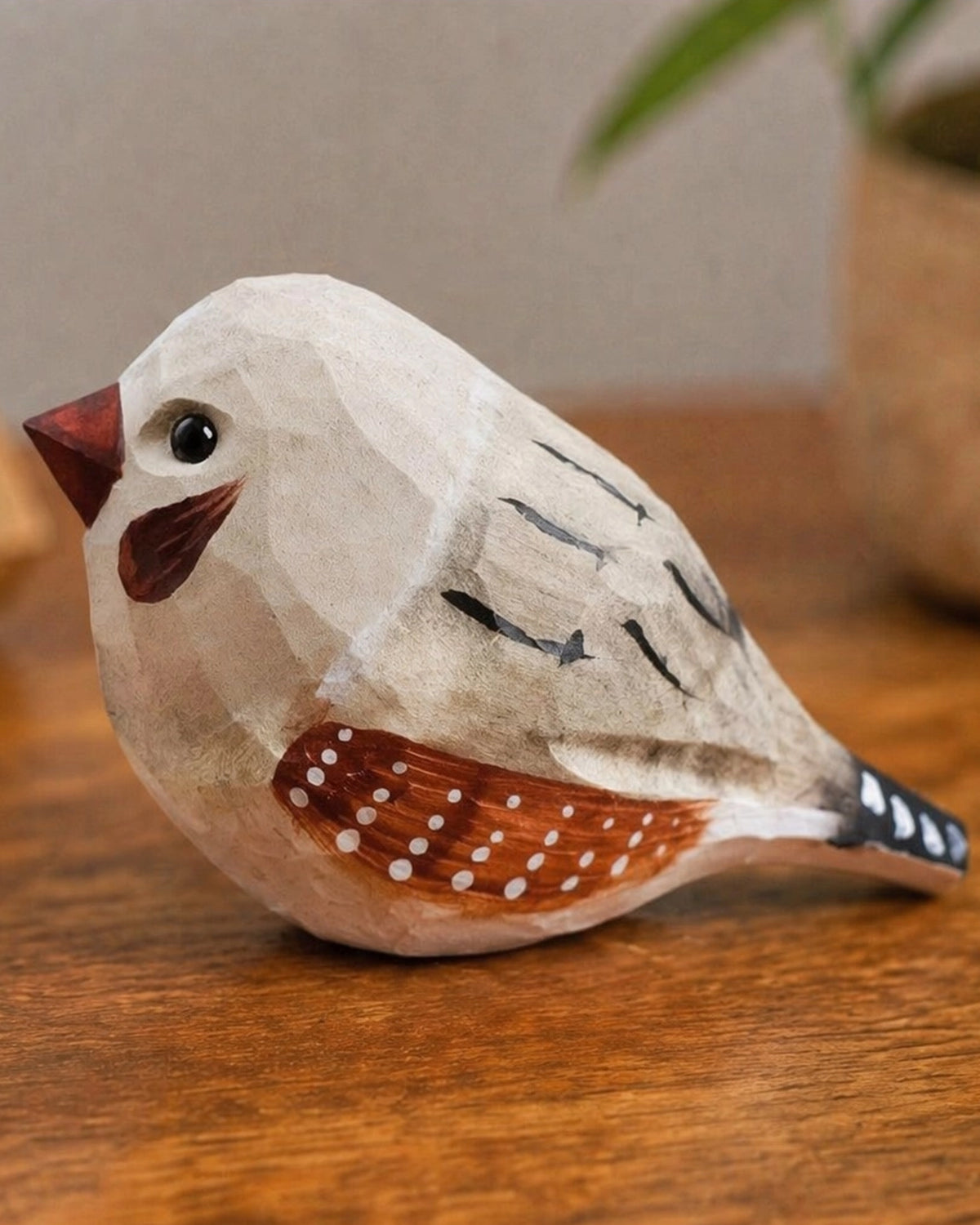 Gray hand-painted carved wood bird by Faire on a brown surface with nature-inspired background accents.