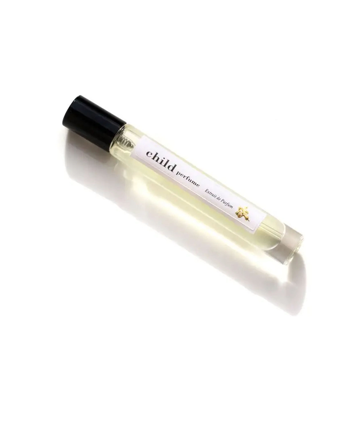 A clear glass roll-on bottle of Faire’s Child Perfume Extrait de Parfum with a black cap sits on a white surface. Its label reads “child perfume” in lowercase, featuring fine text and a gold star that evoke this artisanal scent’s allure.