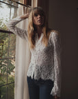 VERONA white floral lace button-down shirt paired with blue jeans, worn by a woman leaning against a window.