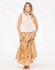 A woman stands barefoot against a white background, wearing the Kerri Rosenthal James Sweater Tank, a light tan floral maxi skirt with ruffles, several bracelets, and a white bandana tied around her neck.