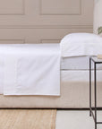 Queen bed dressed in POM POM cotton sateen sheet set with pillow, beside a black metal nightstand at Bungalow Furniture.