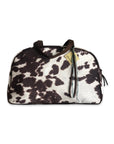 The Faire Oakley Overnighter- Faux Cowhide is a stylish travel bag featuring a brown and white cowhide pattern, black handles, and a tan tag, shown on a white background.