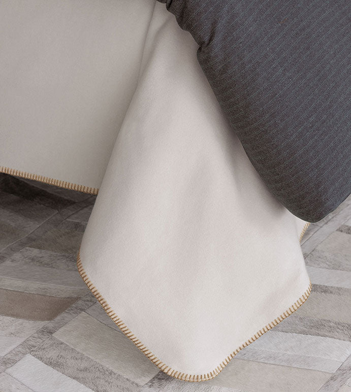 Cream flannel Pattinson Blanket Stitch Coverlet by Eastern Accents, styled next to a dark gray throw on a patterned floor.