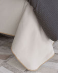 Cream flannel Pattinson Blanket Stitch Coverlet by Eastern Accents, styled next to a dark gray throw on a patterned floor.