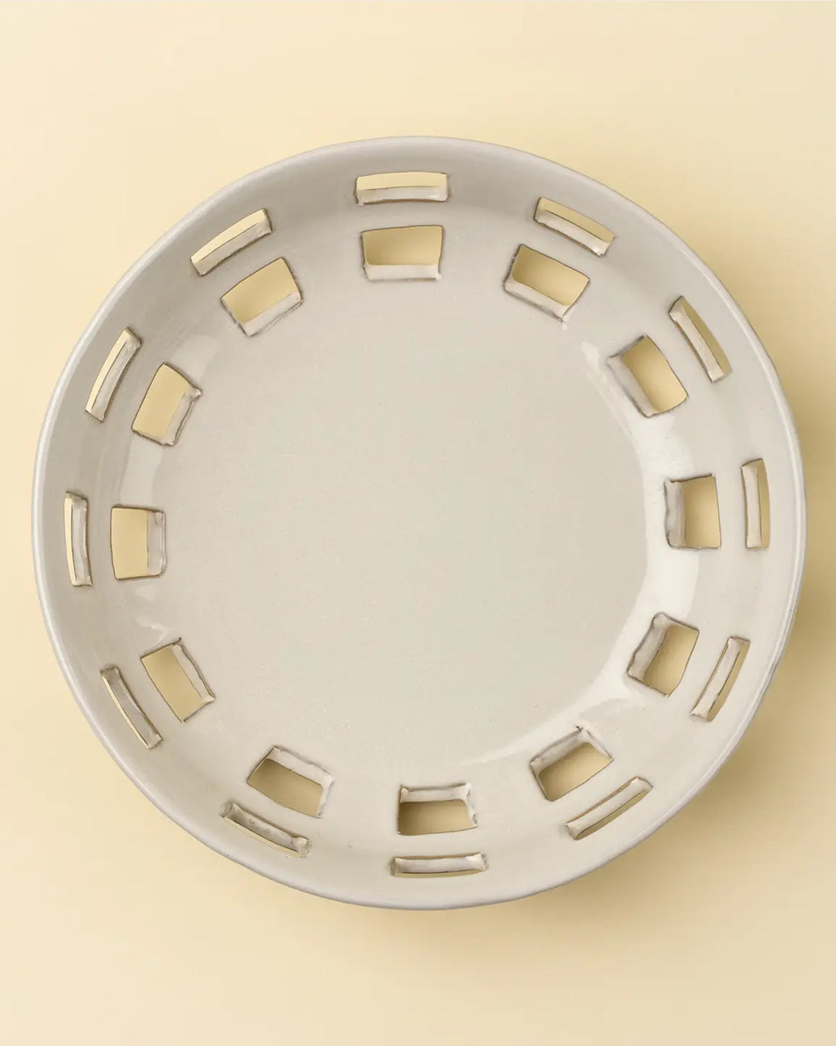 The Cypress Fruit Bowl L by Indaba is a round, off-white ceramic plate with rectangular cutouts around the rim—a stylish kitchen accessory ideal for displaying fruit on any countertop.
