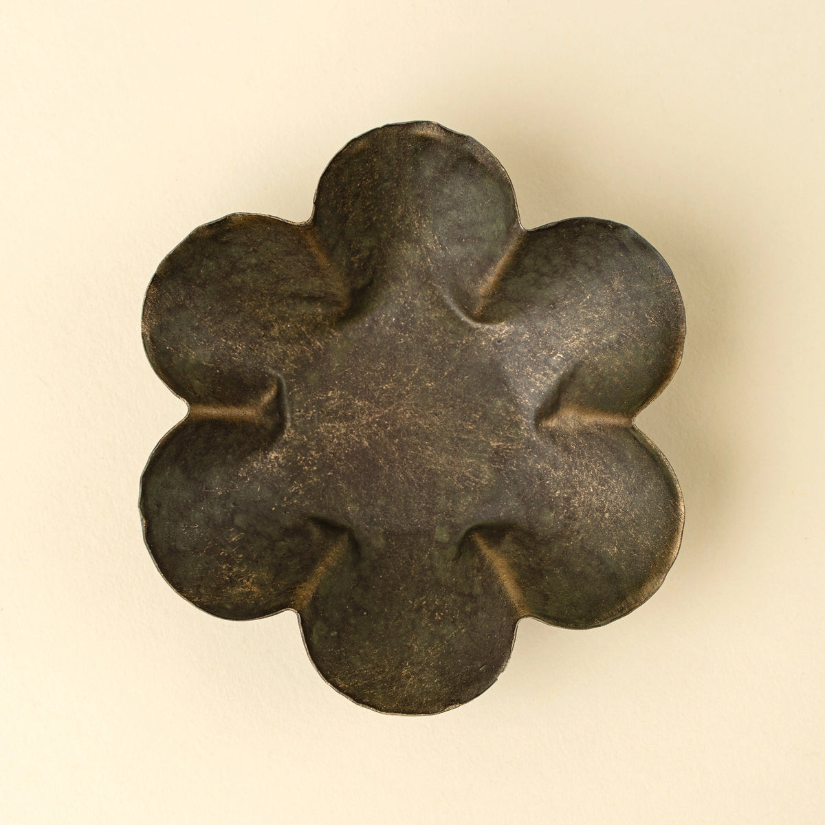 The Faire Florentine Catchall Dish, Daisy, features a dark metallic six-petaled flower design with textured, gently grooved petals and a vintage finish, displayed against a light beige background.