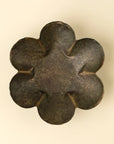 The Faire Florentine Catchall Dish, Daisy, features a dark metallic six-petaled flower design with textured, gently grooved petals and a vintage finish, displayed against a light beige background.