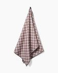 The Faire Chic Checker Yoga Towel in pink and beige checkered pattern with black trim hangs from a hook against a plain white background.