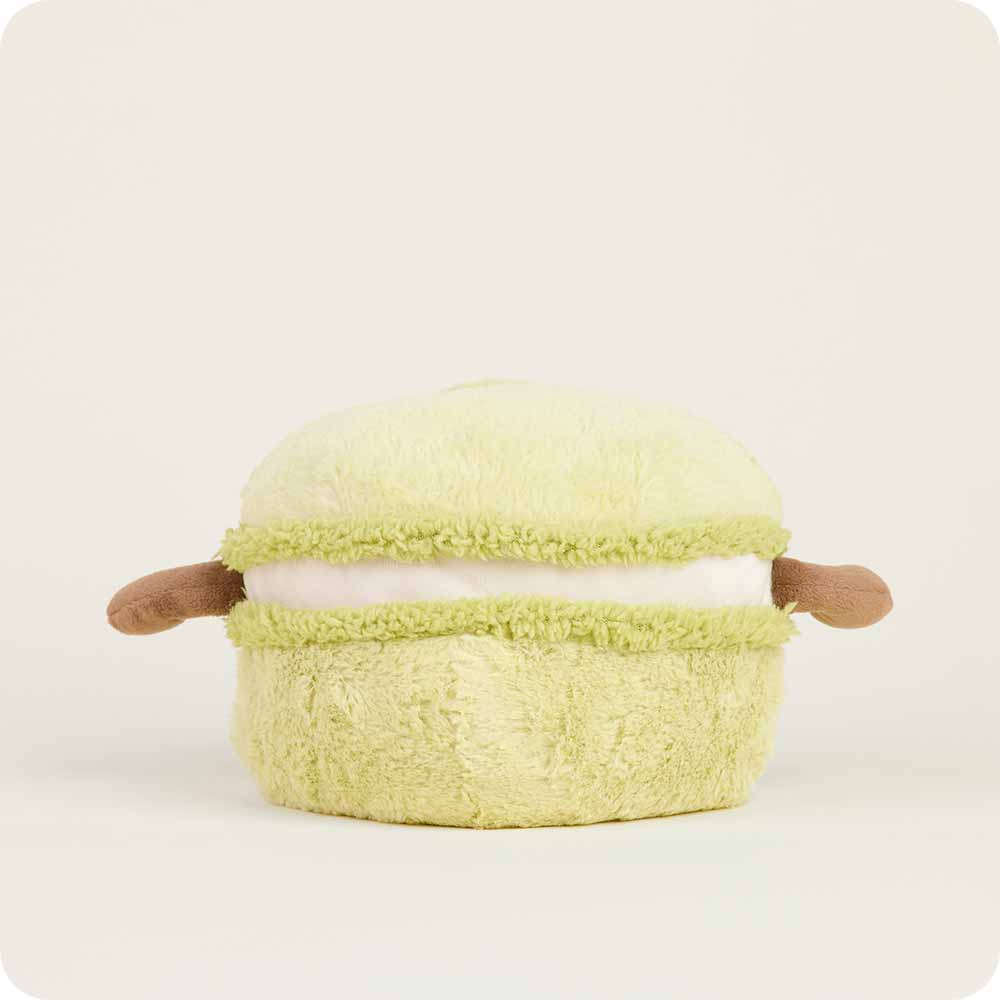 The Faire Green Macaroon Warmie is a light green, microwavable plush toy with small brown arms for sensory comfort, shown against a plain off-white background.