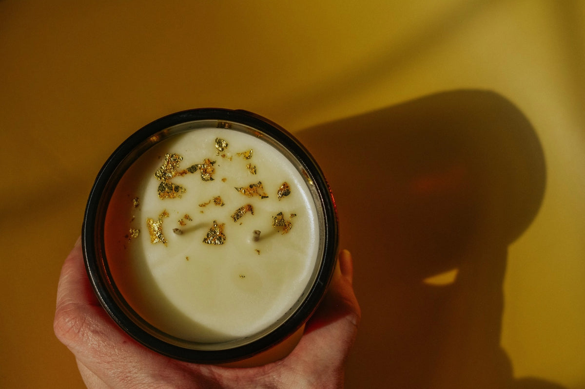 Faire Gold Dust Woman Candle with a creamy gold-flecked drink, styled on a vibrant yellow surface for Bungalow ambiance.
