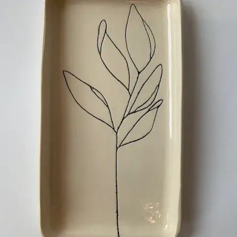The Floral Small Tray by Faire is a rectangular cream ceramic piece featuring a minimalist hand-etched black line drawing of a leafy plant stem in the center, adding botanical style and detail.