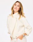A woman with light brown hair confidently poses against a white background, hands in her pockets, wearing the Kerri Rosenthal Denim Jacket / Cloud with rolled sleeves and a silver watch.
