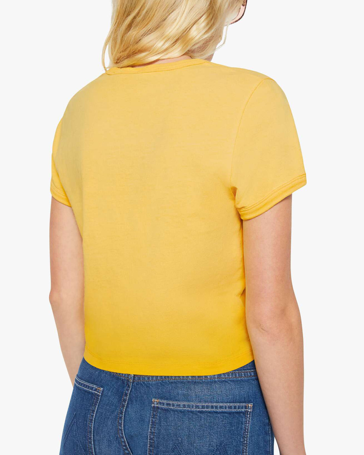 A person with long blonde hair is shown from the back, wearing Mother’s The Itty Bitty Ringer yellow 100% cotton short-sleeve t-shirt and blue jeans against a plain white background.