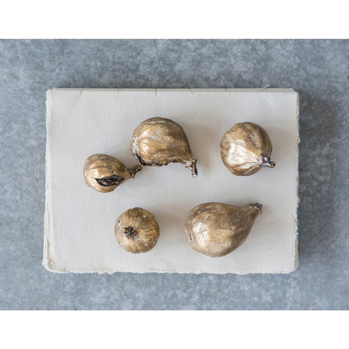 Set of five gold fig sculptures by Creative Co-op displayed on white paper atop a gray textured surface.