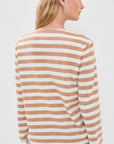 A woman with long blonde hair and gold hoop earrings wears the Denimist MILLS POND STRIPED T in beige and white stretch jersey with light blue jeans, standing with her back to the camera.