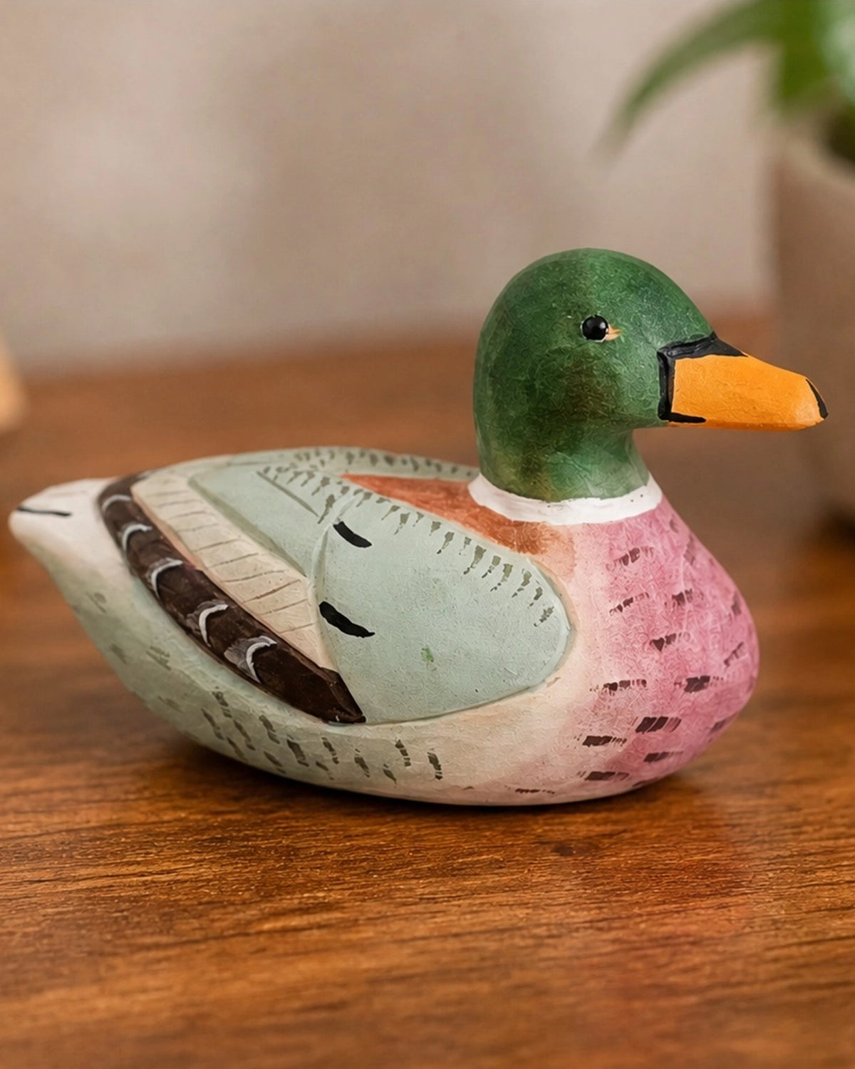 Pink hand-painted carved basswood duck by The Faire on wood with a softly blurred plant background.