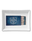 The Faire Ceramic Tray is a rectangular white ceramic trinket tray with a blue matchbook labeled "Paris Ritz Hotel" and matches on the right—ideal for organizing small items or giving as a stylish gift.