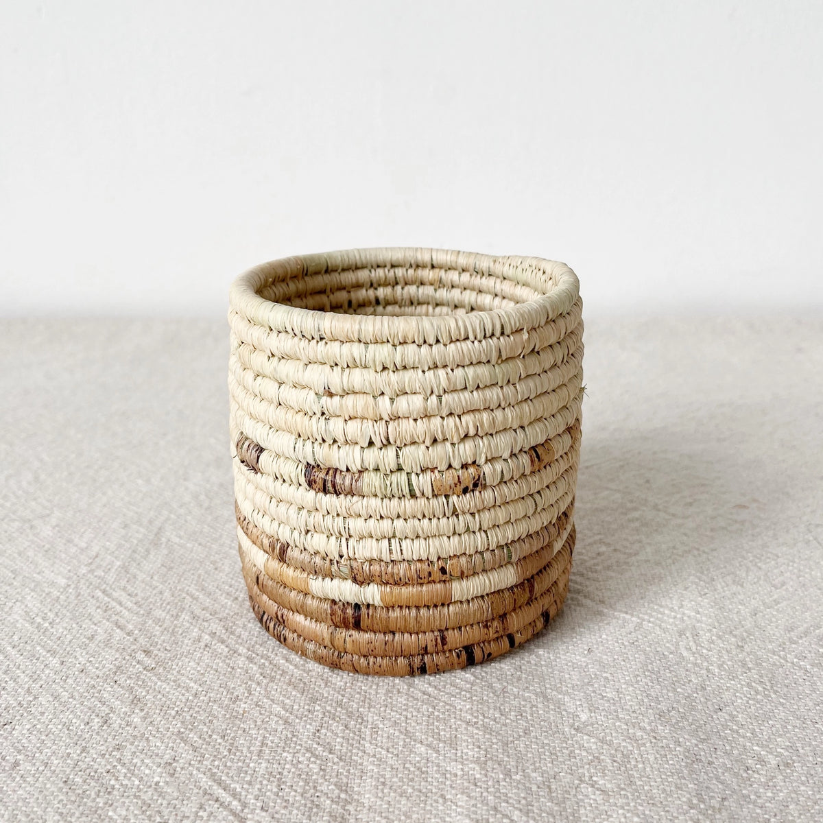 Small round basket with natural and brown stripes, handmade by Faire, Mkongo style, textured surface.