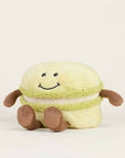 The Faire Green Macaroon Warmie is a microwavable plush toy shaped like a light green macaron with a smiling face, brown arms, and legs, offering sensory comfort against a plain light background.