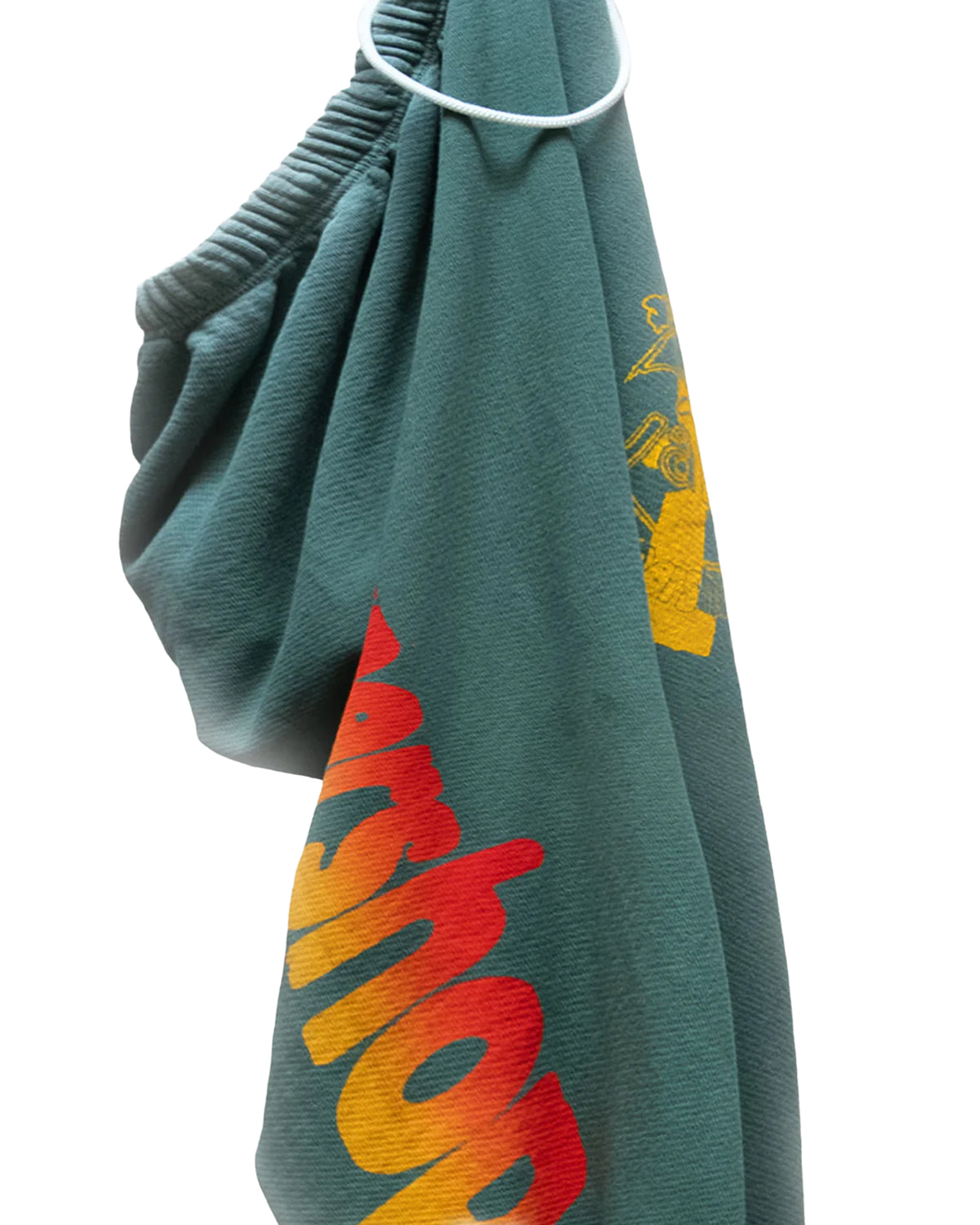 A green Artyard Yumm OG Sweatpant by Free City (sparrow, LLC) with yellow and red partially visible text, hand-screen printed, is shown hanging on a white plastic hanger against a white background.
