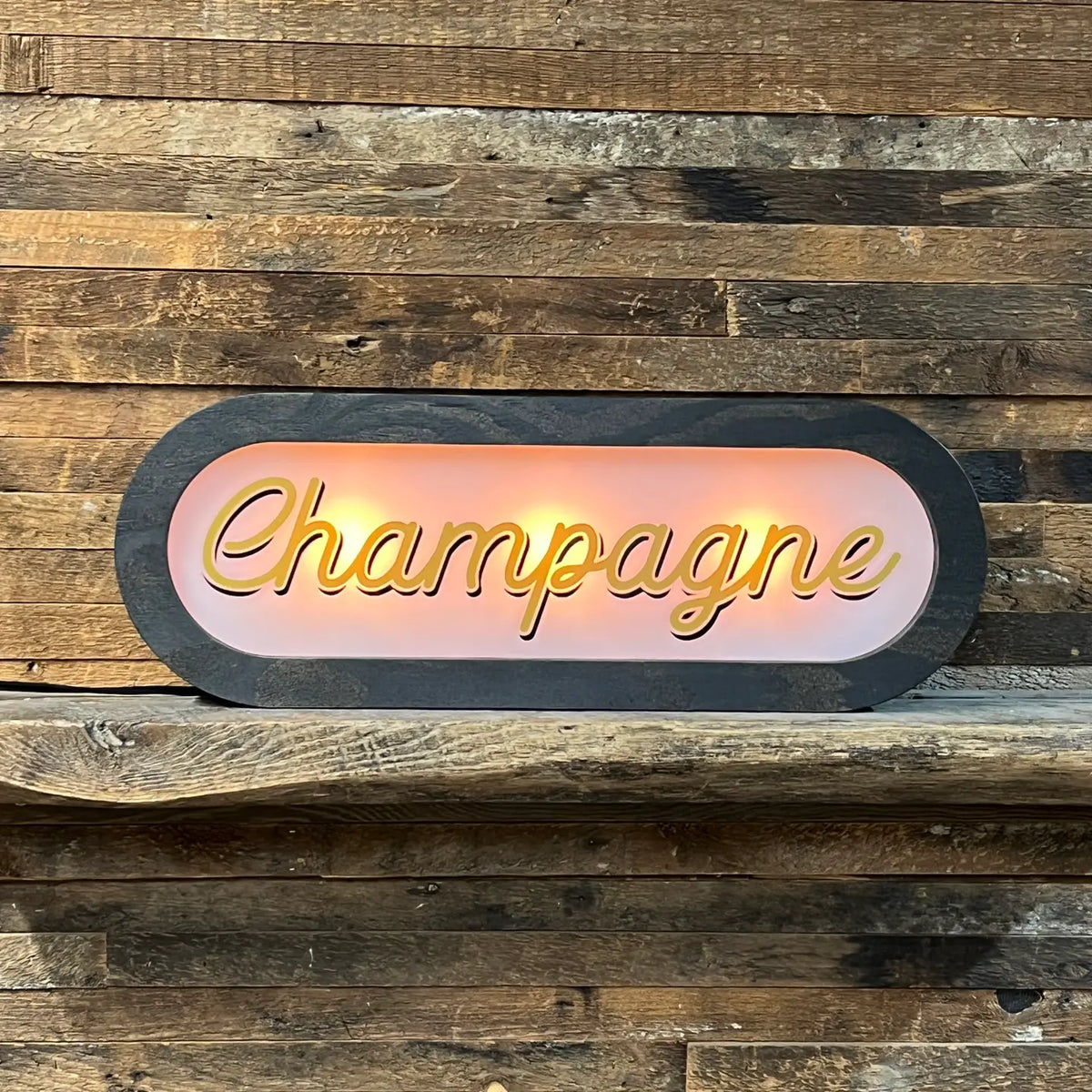 The Faire Lighted Sign features the word "Champagne" in cursive neon, glowing against a rustic wooden wall—ideal as personalized wall decor or a custom illuminated sign for your space.