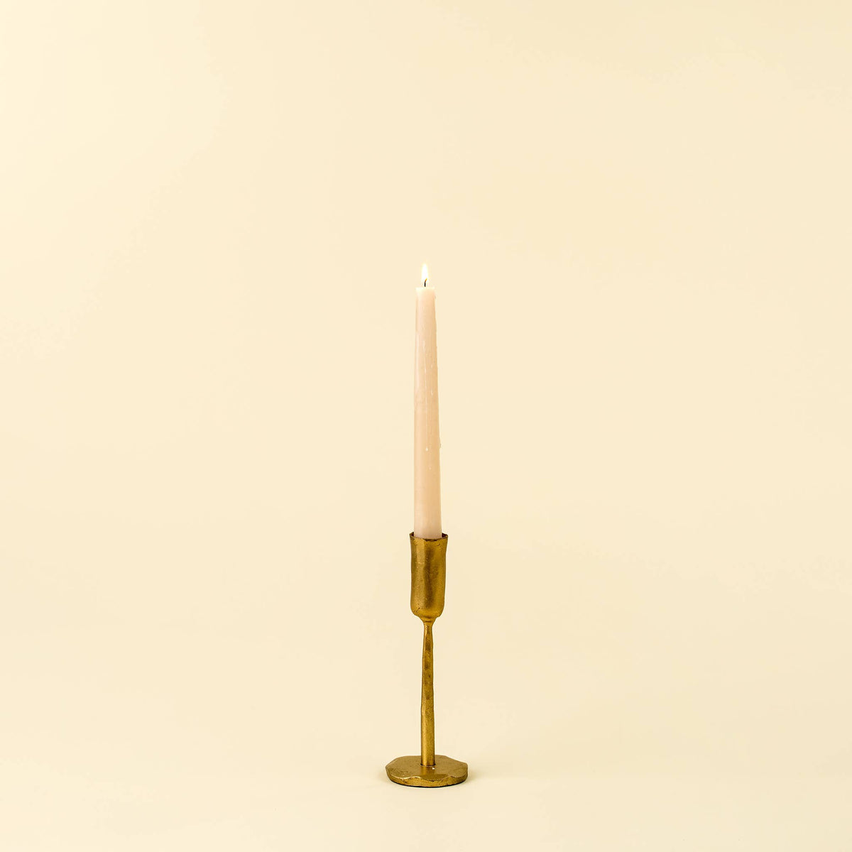 Gold Faire Luna Forged Candlestick S holding a pink taper candle, shown against a neutral beige background.