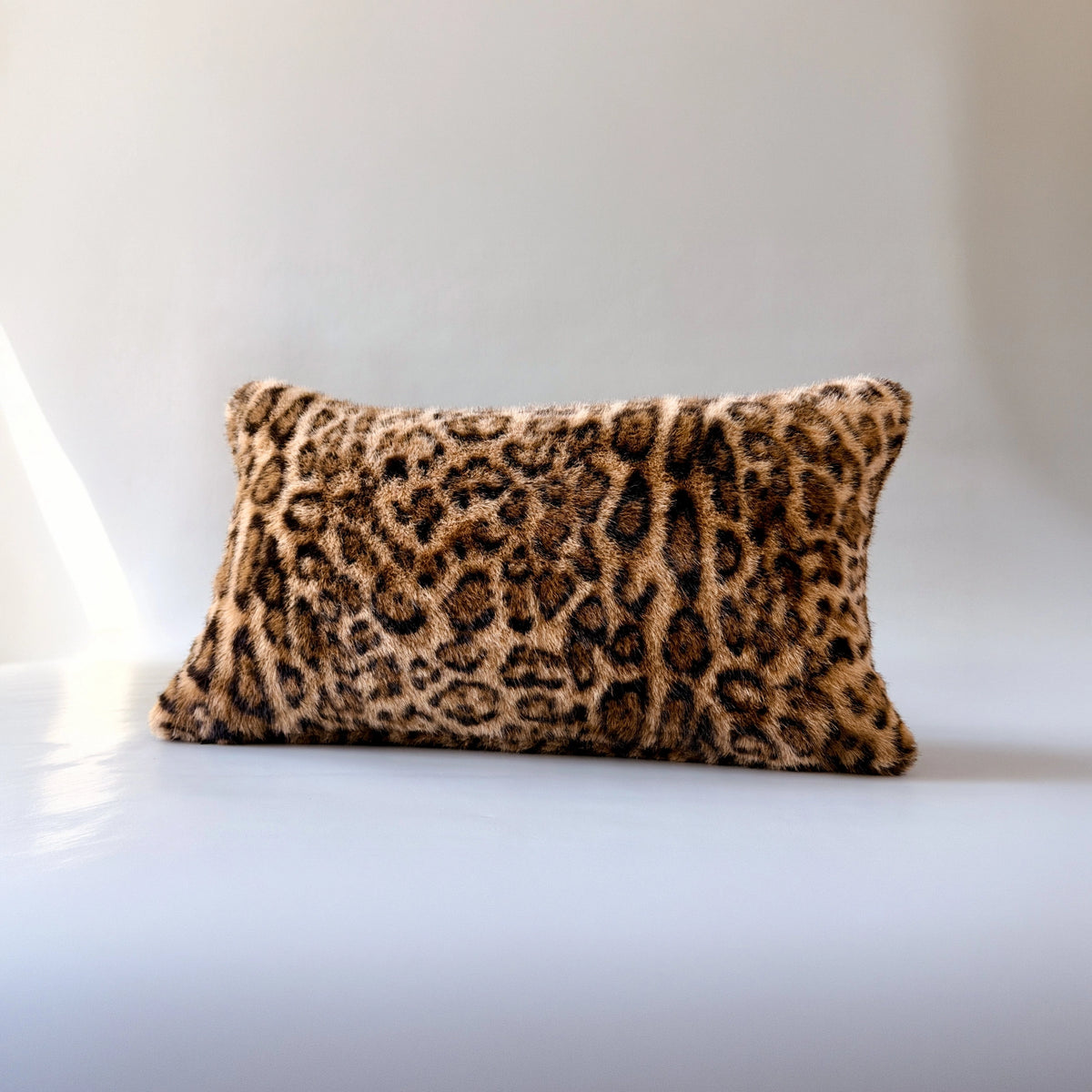 Leopard print lumbar pillow with plush faux fur cover by Faire, shown on a sleek white surface.