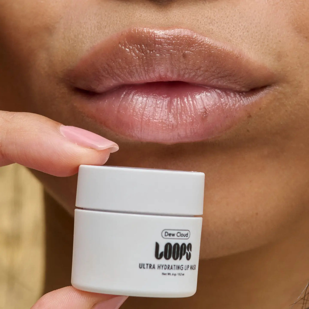 A close-up of lips with a glossy finish shows a small white jar labeled "Faire Dew Cloud Mini Lip Mask" near the mouth, highlighting this ultra-moisturizing, hydrating lip treatment.