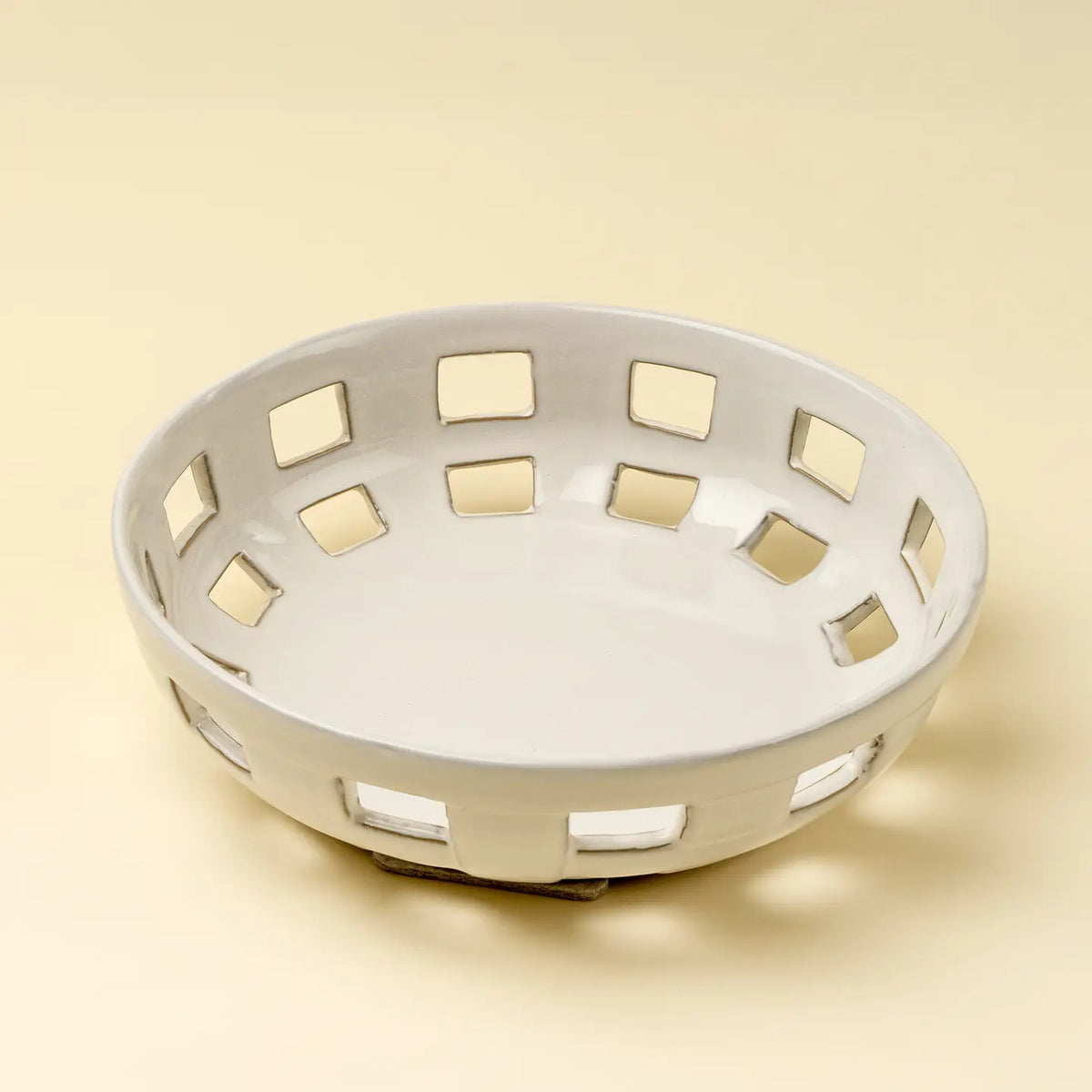 The Indaba Cypress Fruit Bowl L is a round, white ceramic bowl with square cutout patterns—an elegant kitchen accessory shown on a light beige background.