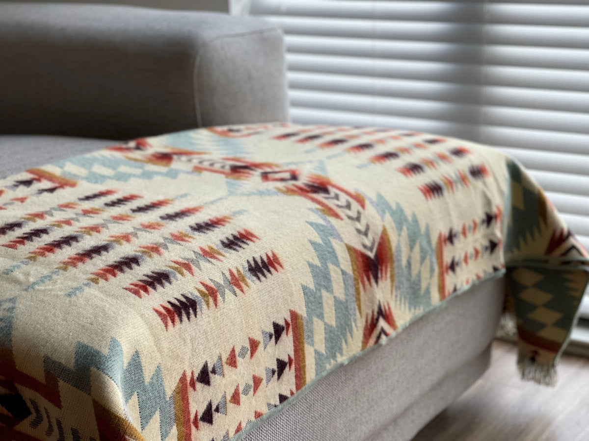 Secoya Throw in Vibrant Mint, a multicolored geometric blanket draped on a gray sofa at Bungalow Furniture &amp; Accessories.