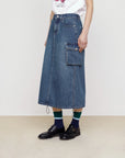 Model wearing Faire’s Pocket Denim Half Skirt styled with a white T-shirt, black shoes, and navy-green striped socks for an effortless street look against a plain backdrop.