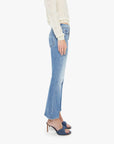 A person stands sideways against a white background, wearing Mother’s The Outside Flood vintage blue cropped flare jeans, a cream long-sleeve top, and blue heeled sandals.