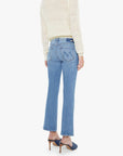 A person wearing Mother’s The Outside Flood vintage blue straight-leg jeans and a sheer cream sweater stands facing away, also wearing blue heeled mules.