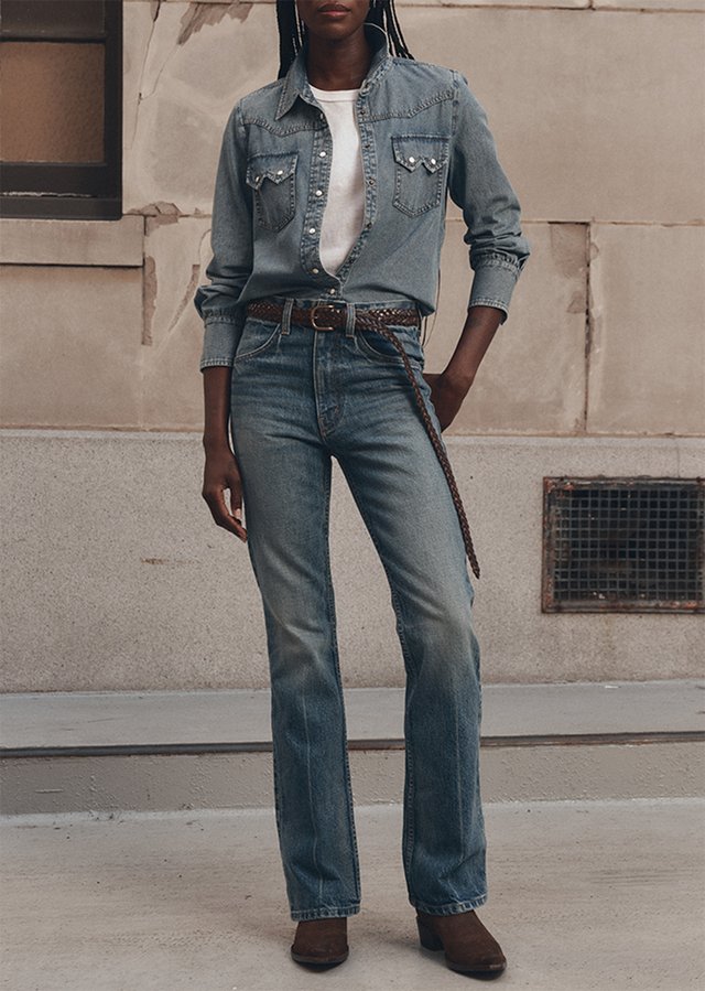Model wearing a fitted denim Western shirt and flared jeans with a dark belt and brown shoes.