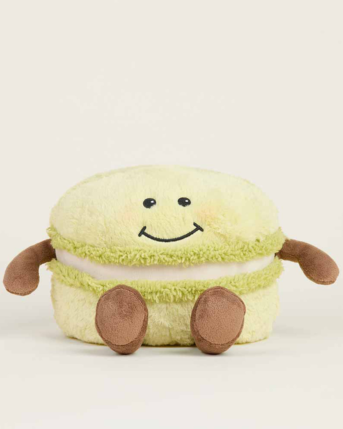 The Faire Green Macaroon Warmie is a light green plush toy shaped like a macaron with a smiling face, brown arms and legs. This microwavable plush offers sensory comfort for cozy relaxation.