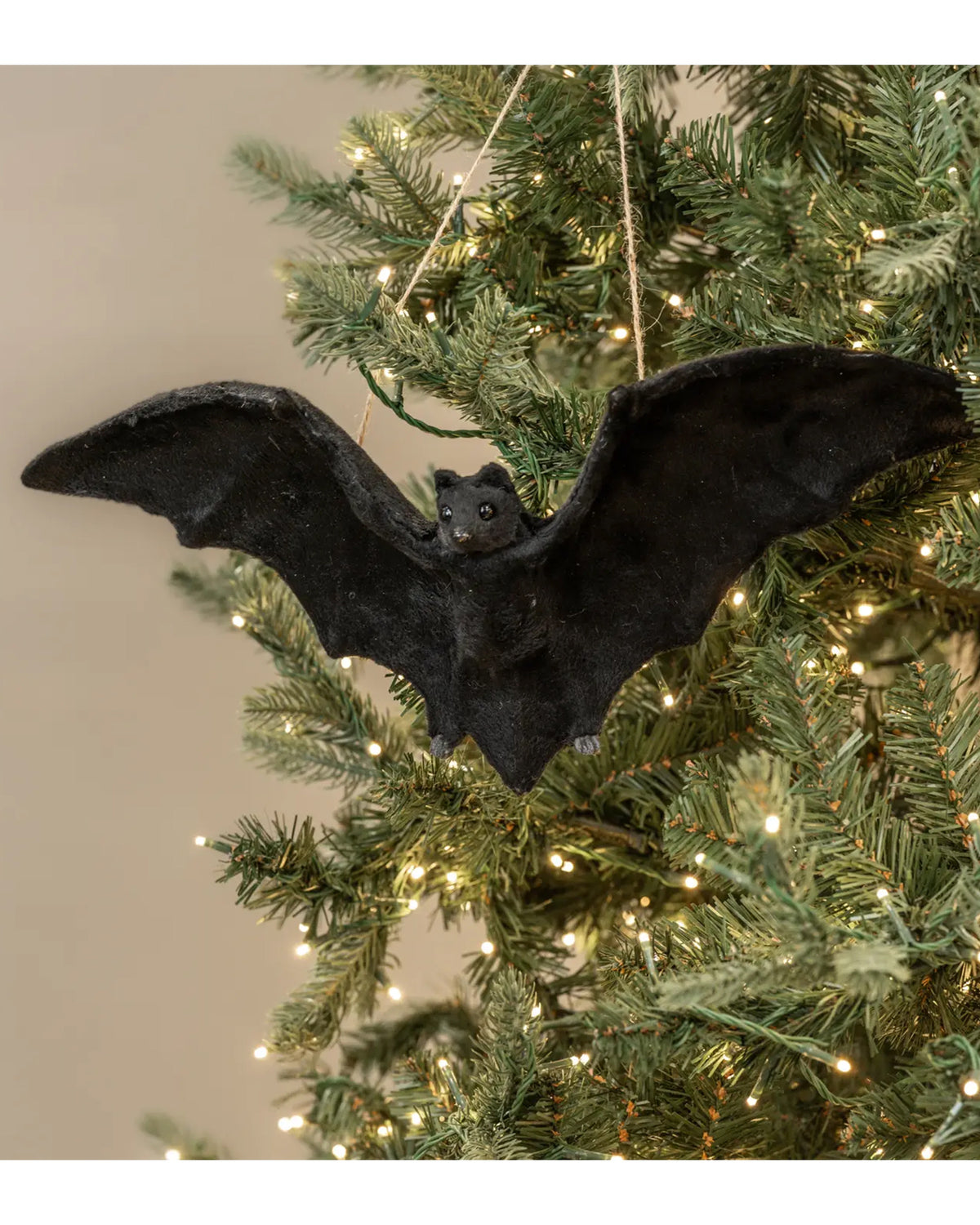 16.75″ Faire Bat Ornament on a lit Christmas tree, green branches in background, Bungalow Furniture & Accessories.